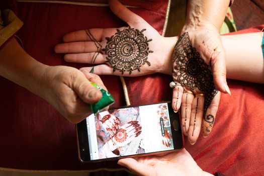Woman getting a henna tattoo mehendi design copied from phone onto her hand for the bride bridesmaid shaadi event or a hindu festival like karwachauth diwali holi and teej