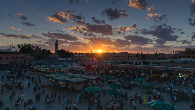 Yamaa el Fna Square with its markets and crowds of people and the tower of the mosque in the background, at sunset. Travel concept. Marrakech, Morocco