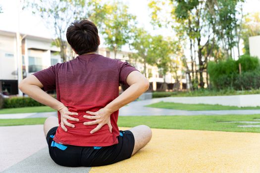 Male athlete suffering from back pain and injury. Hands grab back or waist after running in the park.