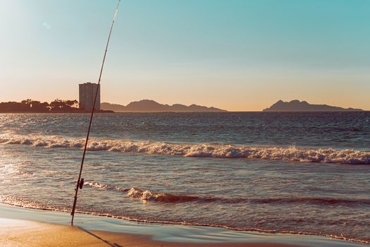 Fishing rod in a beach in front of a massive building during a sunset in spain