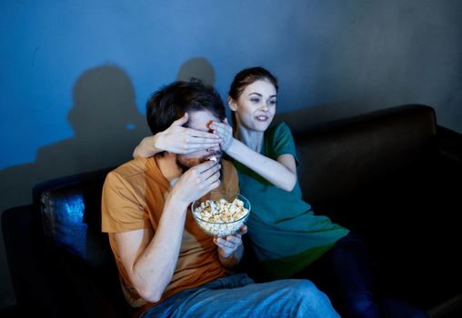 Energetic woman model on a leather sofa and a man popcorn in an evening plate