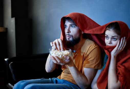 scared woman with a red plaid on her head and a man with a plate of popcorn in a dark room