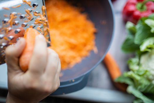 Female hands firmly grating a carrot into a bowl
