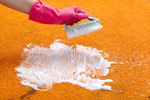 Woman Hand Cleaning Stain On Carpet With hard brush. Orange carpet cleaning. carpet cleaning service concept
