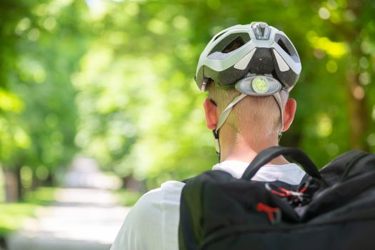 Rear view of unrecognizable man wearing protective helmet on bicycle cycling in city park