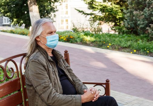 elderly man in protective mask sits on a bench in a city park