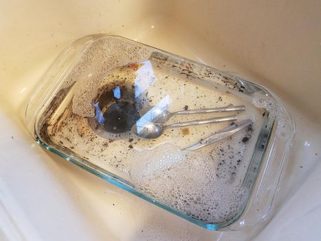 dirty glass tray with water in sink with silverware utensils