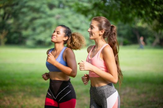 Happy young curvy women jogging together in park. Healthy girls friends running on the city street to lose weight.