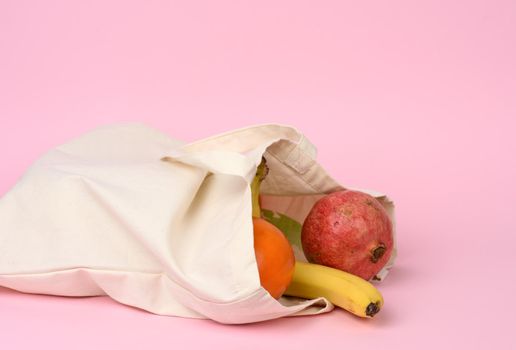 beige textile bag with fresh fruits on a pink background