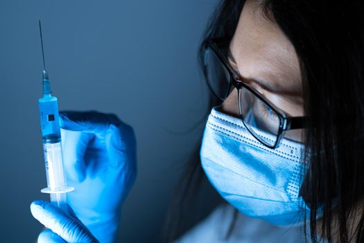 Young female doctor in a medical mask and gloves holds a syringe with a coronavirus vaccine and a vaccine chip inside. Conspiracy theory. Chipping people