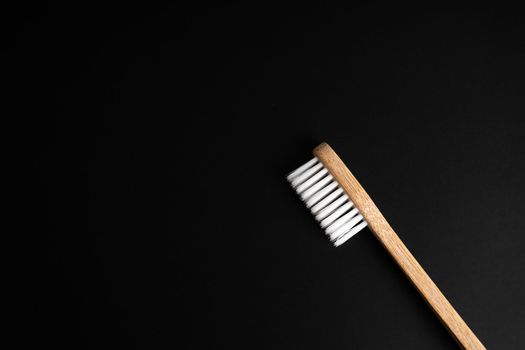 Eco-friendly antibacterial bamboo wood toothbrush with white bristles on a black background. Taking care of the environment is trending. Copy space