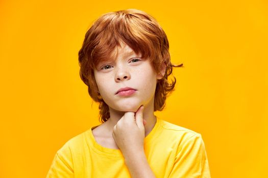 Red-haired boy suspicious look on the chin close-up studio yellow t-shirt