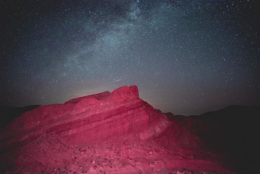 A rock lit up by pink light glowing under the desert sky.