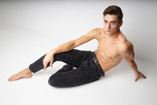 young guy with naked torso sitting on the floor isolated background modern style