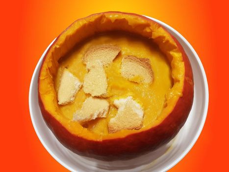 Spicy pumpkin soup with ginger and onions, served in pumpkin with pumpkin. Pkin oil, seeds and croutons on the Halloween background. This is a german version of pumpkin soup