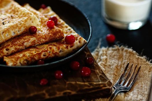 Delicious home-cooked food. Pancakes in a frying pan with cranberry berries and milk. National Russian cuisine. Rustic style