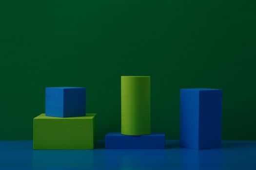 Still life with green and blue geometric figures on blue table against green background with space for text