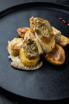 Baked potato and artichoke with fennel al forno, on black textured background