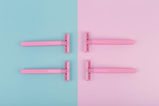Flat lay with four pink plastic razors on pink and blue background