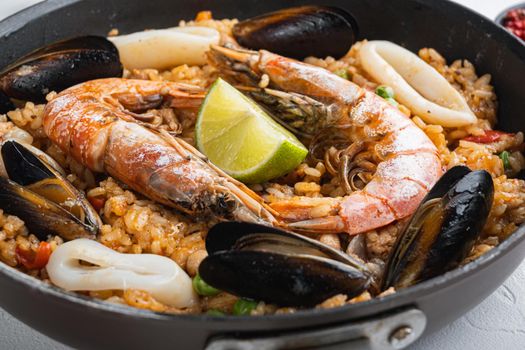 Paella cooked in frying pan on white textured background