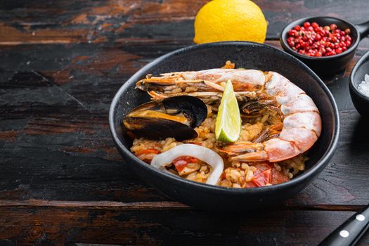 Homemade freshly prepared paella with king prawns, mussels and squid in black bowl on old dark wooden background with copy space