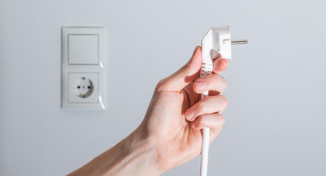 Energy concept: Plug, ready to connect. White cable and plug socket in the blurry background