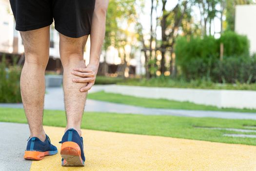 Male runner athlete leg injury and pain. Hands grab painful leg while running in the park.