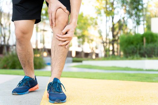 Male runner athlete leg injury and pain. Hands grab painful knee while running in the park.
