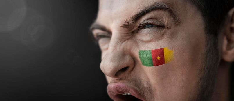 A screaming man with the image of the Cameroon national flag on his face