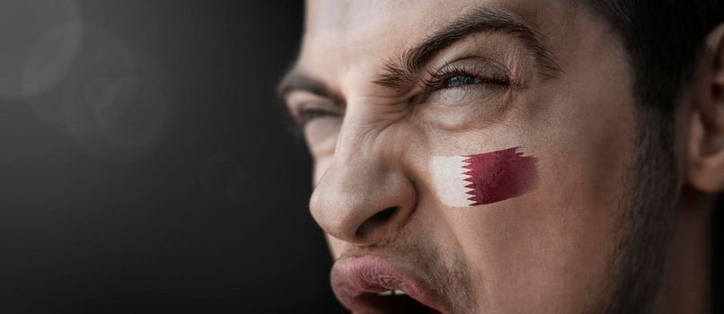 A screaming man with the image of the Qatar national flag on his face
