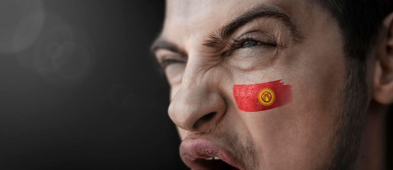A screaming man with the image of the Kirghizia national flag on his face