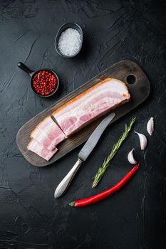 Smoked bacon, whole slab with herbs on black background, top view