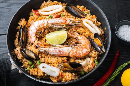 Homemade spanish seafood paella in frying pan and black bowl on black wooden background