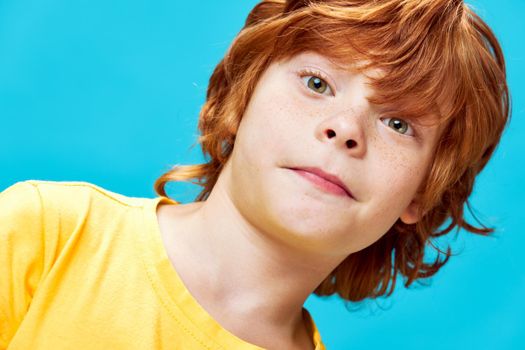 Red-haired boy with freckles face close-up blue background studio