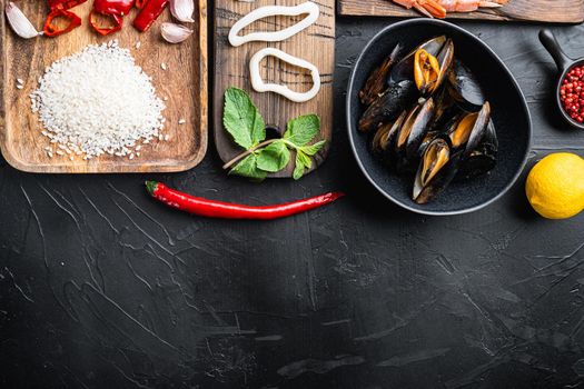 Ingredient for a spanish seafood paella with rice, pea,pepper and shellfish on black textured background, top view with space for text
