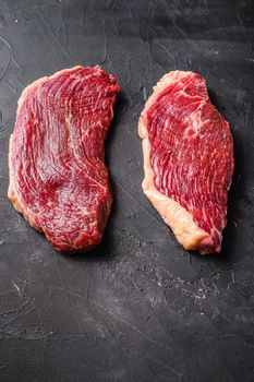 Organic raw picanha beef steaks, on black textured background, side view.
