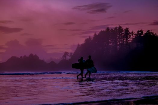 Vancouver Island Tofino, sunset at the beach with surfers in the ocean, beautiful colorful sunset with pink and purple colors in the sky at Vancouver Island with pople surfing
