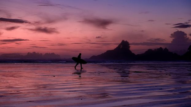 Vancouver Island Tofino, sunset at the beach with surfers in the ocean, beautiful colorful sunset with pink and purple colors in the sky at Vancouver Island with pople surfing