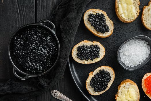Canapes with black sturgeon caviar, on black wooden table background, top view flat lay