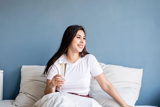Young brunette woman sitting awake in the bed drinking champagne