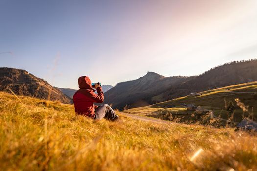 Hiking girl is enjoying the sundown in the mountains, sitting on the ground. Warm colors, alps, Austria