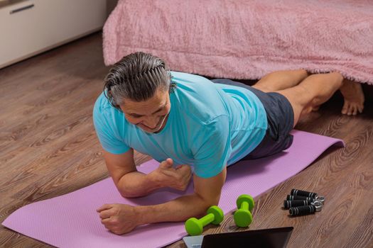 50 year old man performs exercises lying on mat at home looking at computer