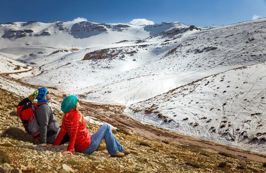 Happy Young Couple Sitting and Resting in the Mountains at Base Camp. Enjoying Adventure Hike in the beautiful Snowy Mountains. Active Sportive Lifestyle. Winter Holidays Concept.