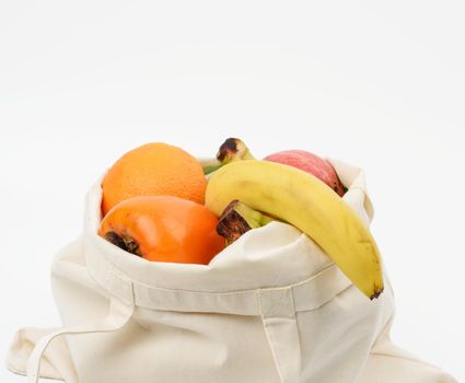 beige textile bag with fresh fruits on a white background, close up