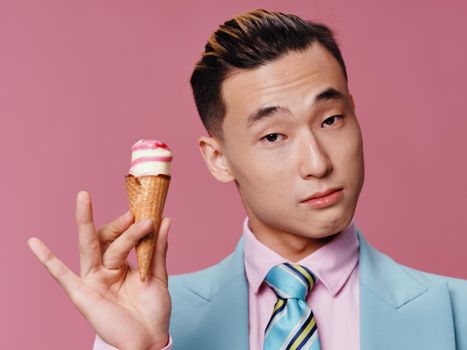 Asian-looking man holding ice cream in blue suit pink background enjoyment