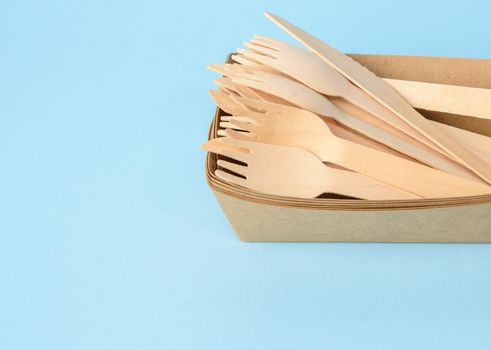 wooden fork and empty brown disposable plate made from recycled materials on a blue background, top view
