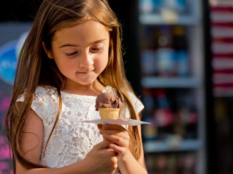 Cute little girl in white dress looks at ice cream.