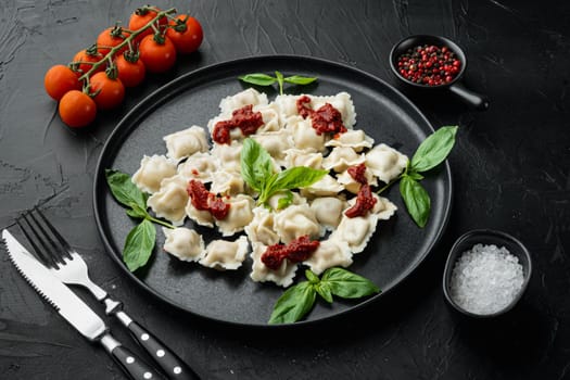 Appetizing ravioli with tomato sauce, cheese and basil with basil parmesan and tomatoe on black plate, on black background