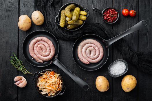 Wurst or Bratwurst with Fermented Cabbage, Pickled Cucumbers, and Spices in cast iron frying pan, on black wooden table background, top view flat lay