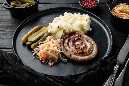 Wurst or Bratwurst with Fermented Cabbage, Pickled Cucumbers, and Spices, on black wooden table background